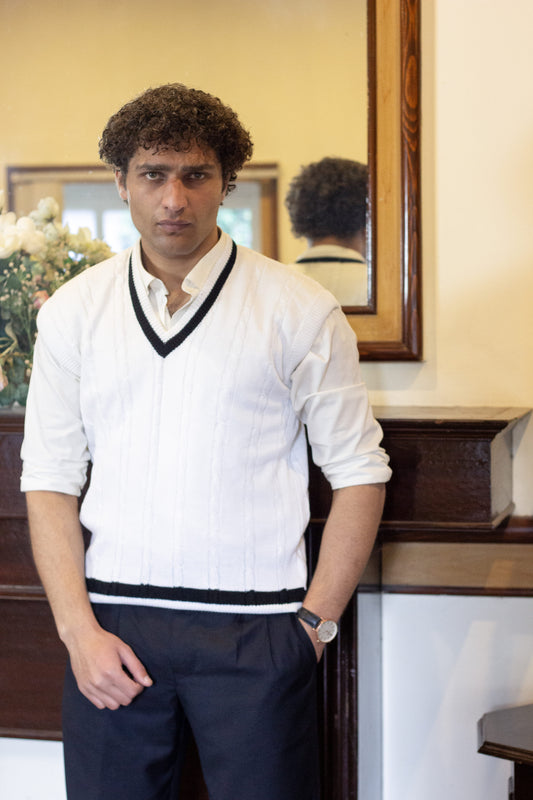 Man wearing a White Cable knitted Sleeveless sweater over a white shirt and black pants in an vintage old money setting